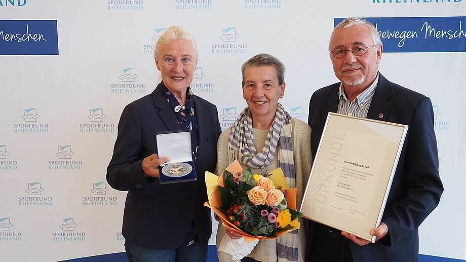 Monika Sauer (links) ehrte Wolfgang Scheib (rechts) für sein jahrzehntelanges Engagement mit der Ehrenplakette des Landessportbundes in Silber. Auch seiner Ehefrau Hanne wurde mit einem Blumenstrauß gedankt.