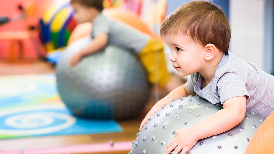 Ein Kleinkind rollt mit seinem Bauch über einen großen Ball.