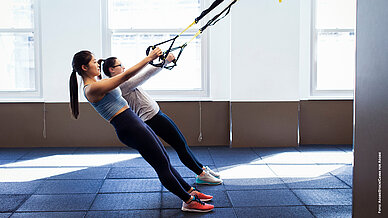 Seitenansicht von Sportlerinnen, die im Fitnessstudio Schlingentraining absolvieren