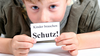 Kind hält ein Schild mit der Aufschrift "Kinder brauchen Schutz" hoch